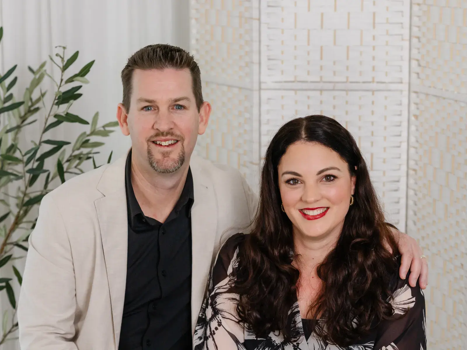 Mathew McCullagh and Shelley Walsh-McCullagh seated side by side, smiling, in front of a woven white screen
