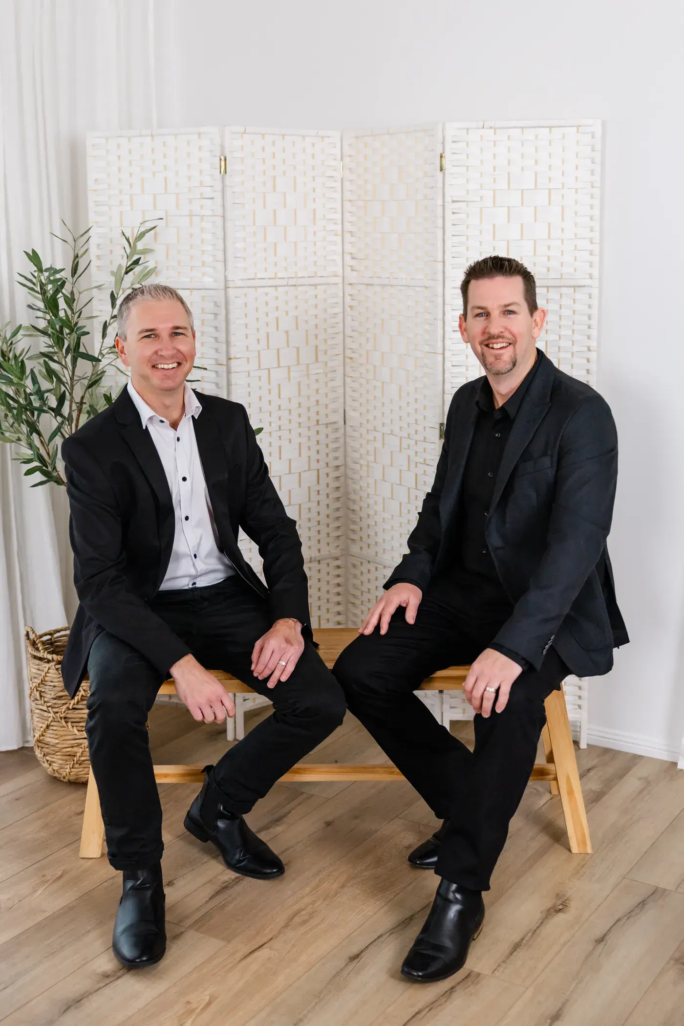 Mathew McCullagh and Jayden Page seated side by side on a timber bench in the Touch Residential studio